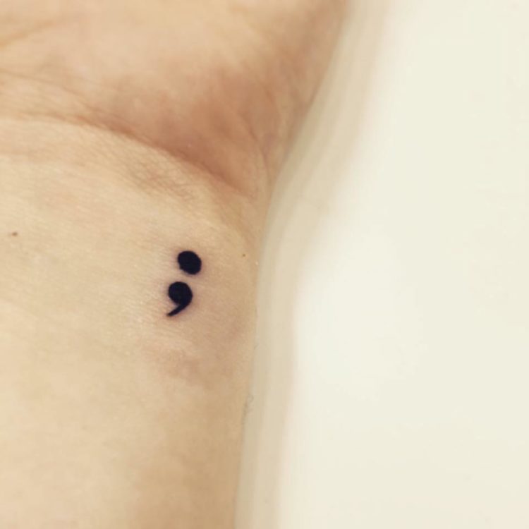 A wrist with a small semicolon tattoo.