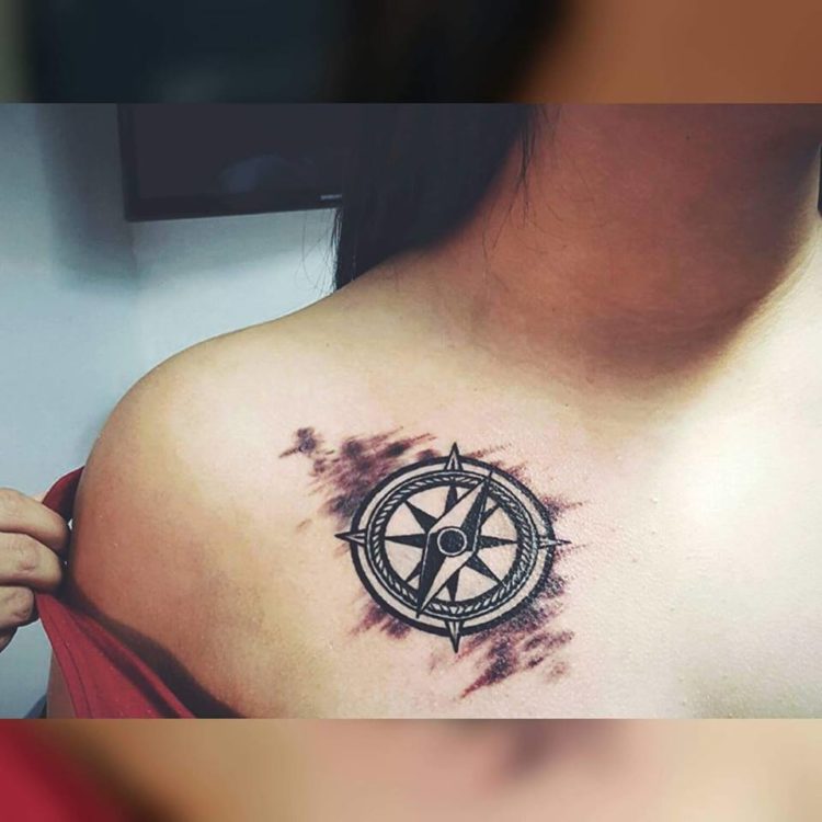 Tattoo of a compass on a woman's chest beneath her shoulder.