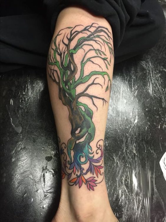 Tattoo on a leg of the tree of life. Brown dying branches of the tree are interwoven with healthy green branches, which also have green leaves and flowers.