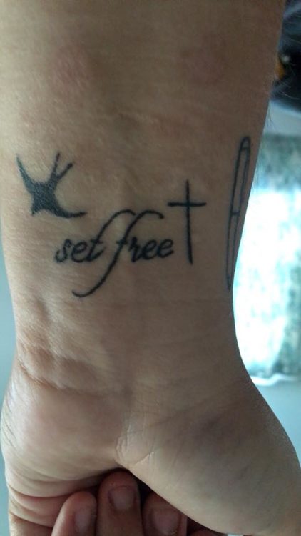 Tattoo of the words "set free" with a cross and a dove in flight.