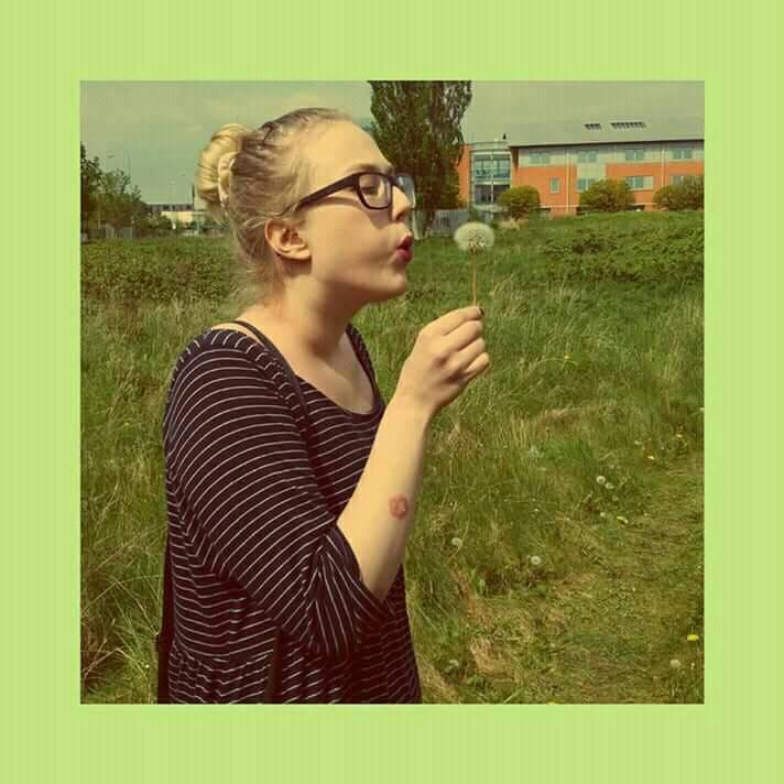 woman standing in a field blowing a dandelion with a patch of psoriasis on her arm