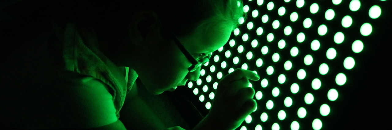 How I Helped My Daughter With a Cortical Visual Impairment Little girl using a LightAide. It is a large board with green lights arranged in rows. She is putting her finger to one of the lights.