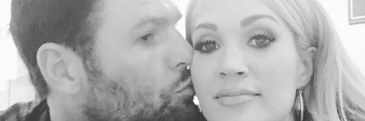Carrie Underwood Opens Up About Her Three Miscarriages Black and white image of Carrie Underwood being kissed on the cheek by husband.