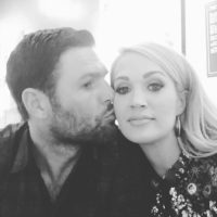 Black and white image of Carrie Underwood being kissed on the cheek by husband.