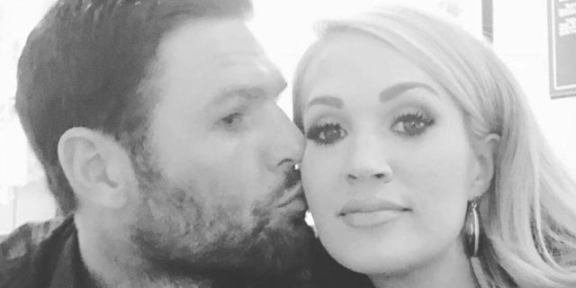 Carrie Underwood Opens Up About Her Three Miscarriages Black and white image of Carrie Underwood being kissed on the cheek by husband.