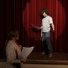Boy acting on stage as teacher watches.
