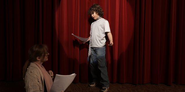 How Drama Classes Helped Me as a Person Who Stutters Boy acting on stage as teacher watches.