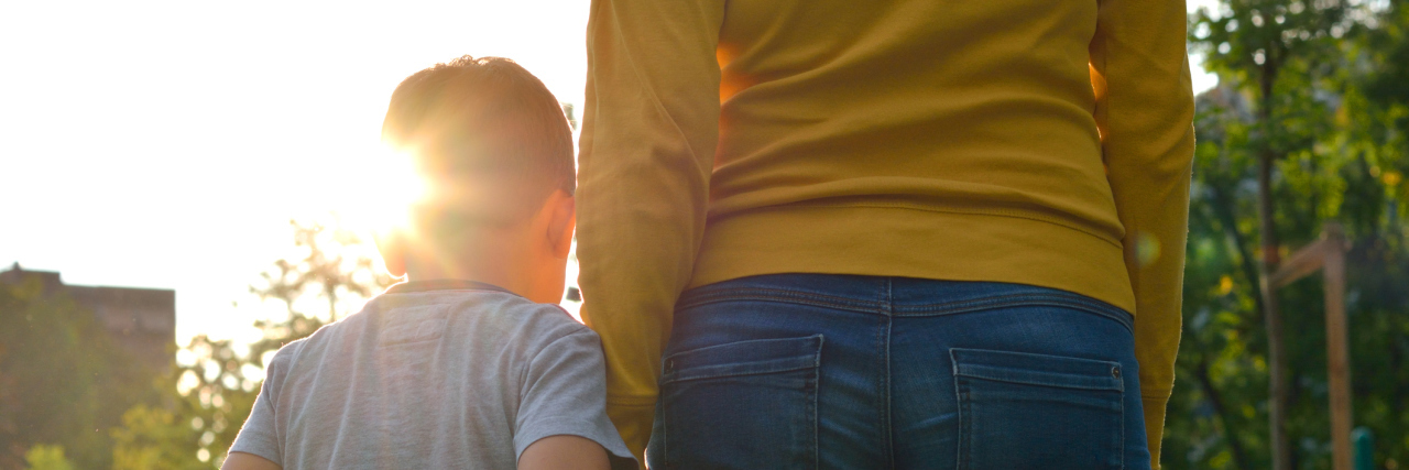 Teaching My Sensory Seeker Child What Consent Means Son holding mom's hand, image of their back at sunset.