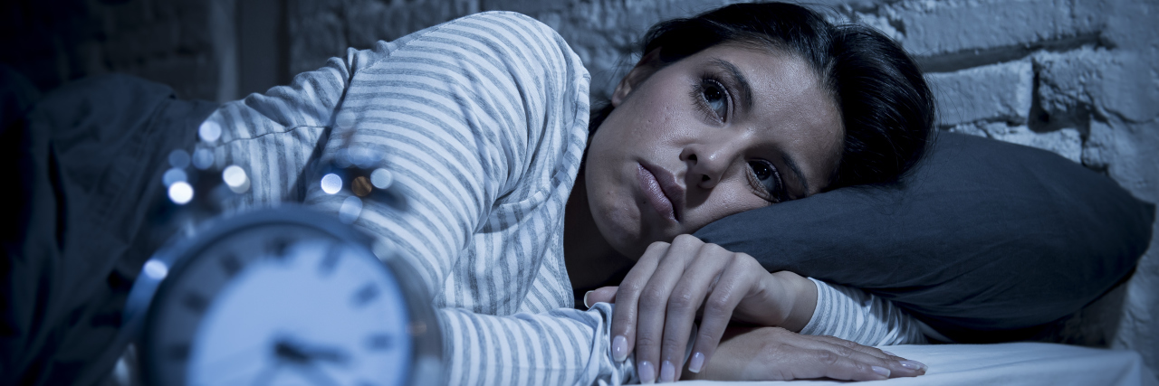 What It's Like Not Knowing If Your Symptoms Are an Emergency woman lying in bed worried