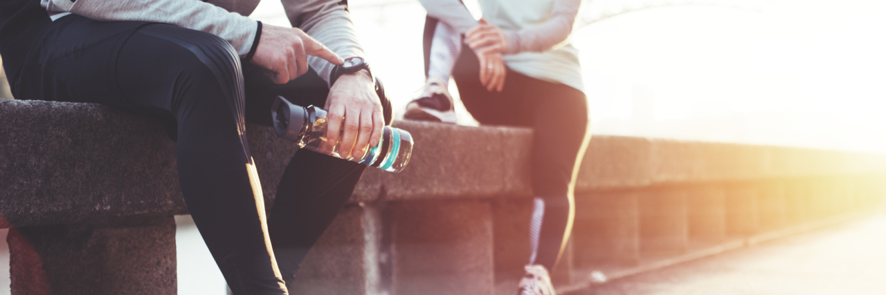 Why Exercise Isn’t Always Helpful With Hashimoto's Thyroiditis Couple of athletes resting after workout session on the street. Tired man with bottle tracking time with his watch and woman relaxing on the bench