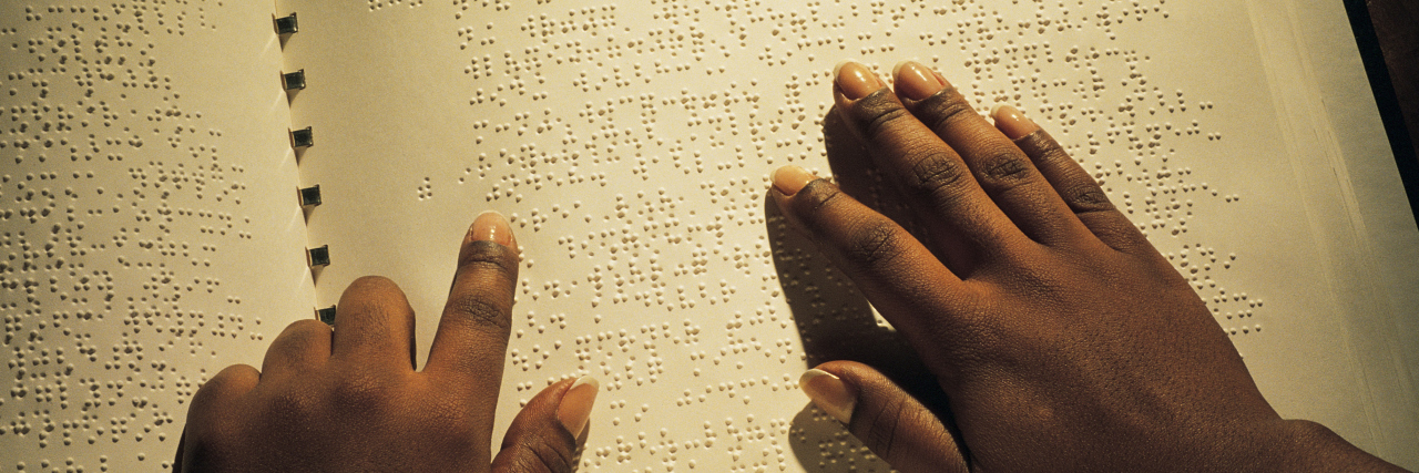 Hands of Black person reading Braille book.