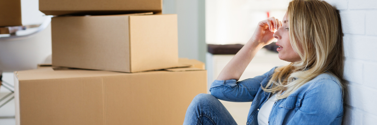 A tired woman sitting on the floor near some unpacked boxes.