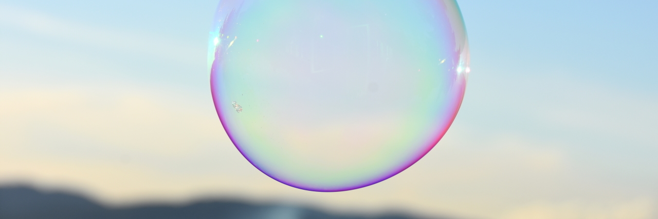 Single bubble with purple outlining floating in a blue sky with a mountain behind it