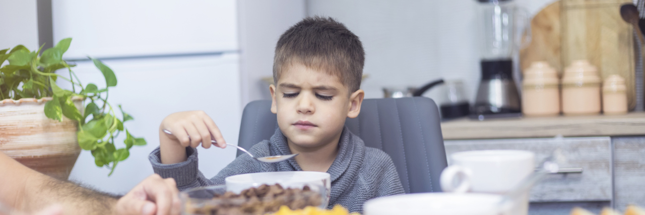 Young boy at dinner table holding spoon and unhapy about the food in front of him as if he does not want to eat.