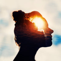 Silhouette of a young woman on a sky background with the sun in her head.