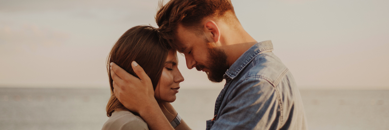 What It's Like Being a Wife With Schizophrenia A couple on the beach. the man embraces the woman's head