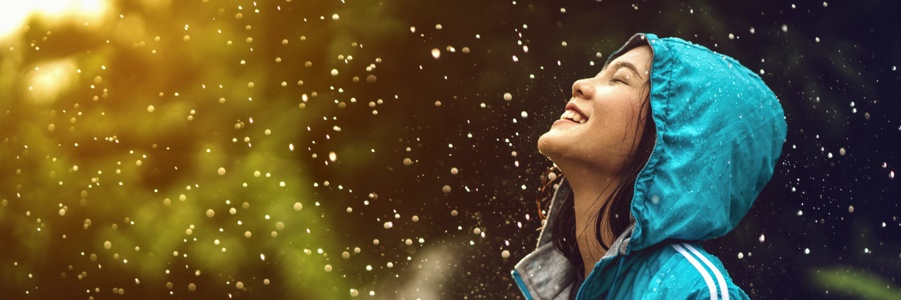 My Truths About Living as an Autistic Person Asian woman wearing a raincoat outdoors. She is happy.