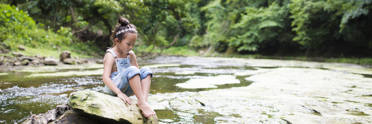 Little girl playing in a stream, daydreaming.