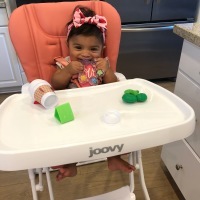 A baby girl sitting in a high chair with toys.