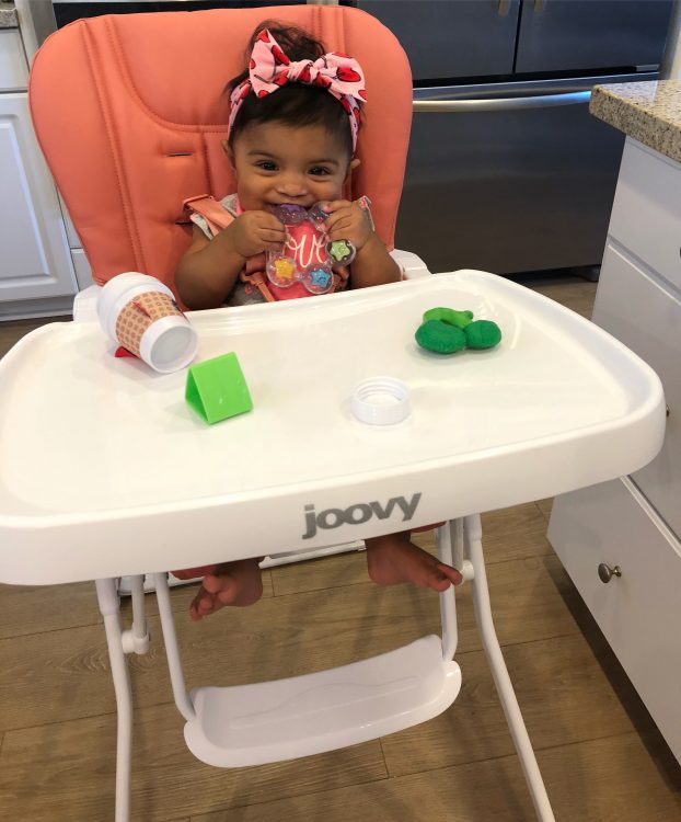 A baby girl sitting in a high chair with toys.