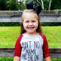 Little girl smiling at camera wearing a shirt that says, "Ain't no mama like the one I got."