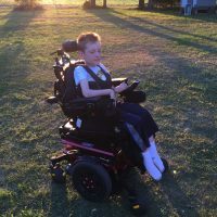 Boy sitting on his powerchair with beautiful sunset behind him.
