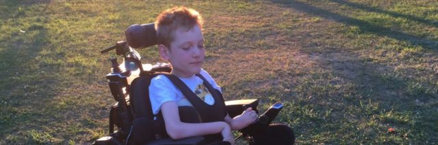 Boy sitting on his powerchair with beautiful sunset behind him.