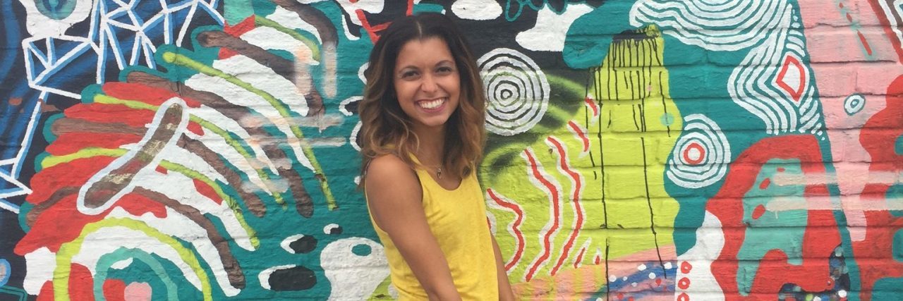 A picture of the writer standing in front of a wall painted with vibrant colors.