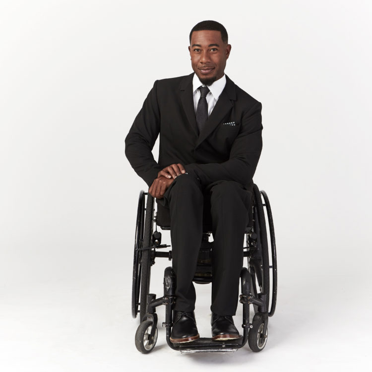 A guy in a wheelchair wearing a black suit.