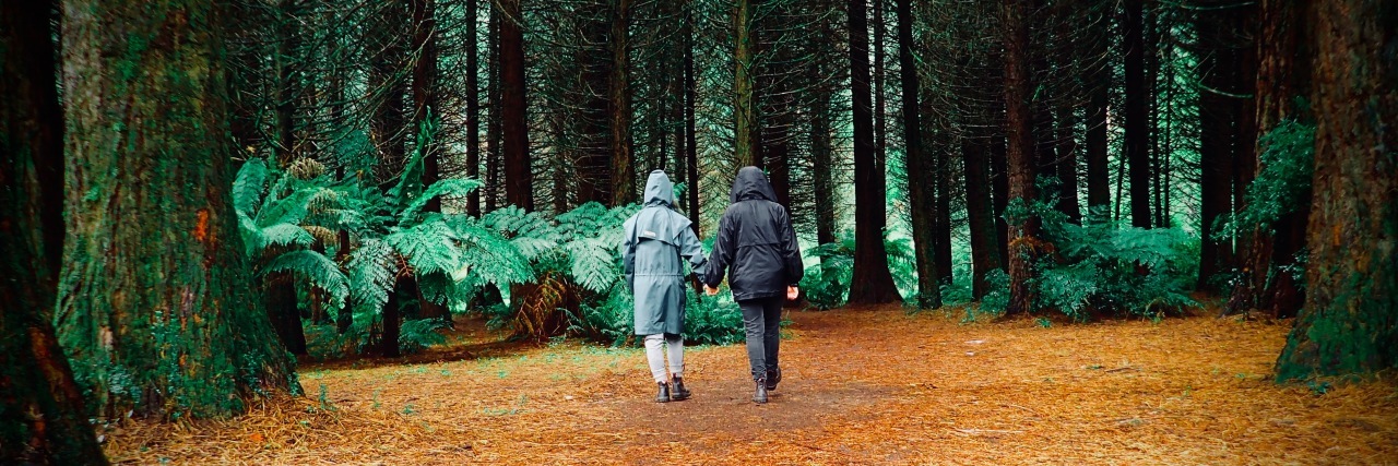 two people holding hands and walking through forest