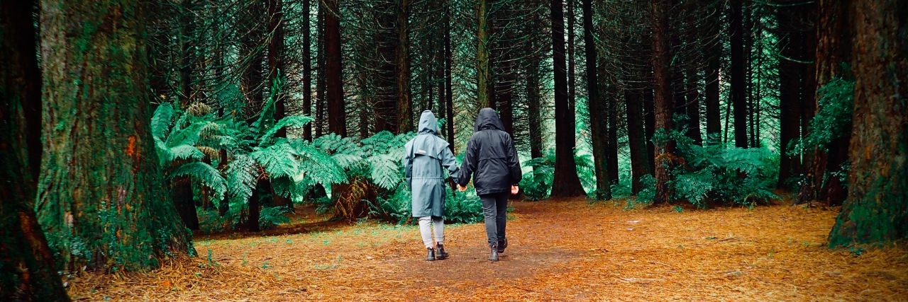 I Have Fibromyalgia, and My Partner Is as Strong as I Am two people holding hands and walking through forest
