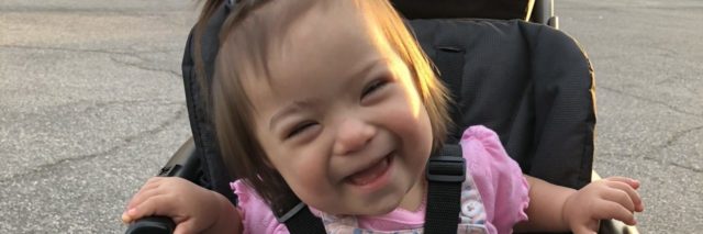 Adorable little girl with Down syndrome sitting on her stroller and smiling at the camera