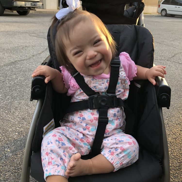 Adorable little girl with Down syndrome sitting on her stroller and smiling at the camera