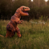 A boy in a T-rex costume is chases a girl dressed like a member of Jurassic Park through a field.