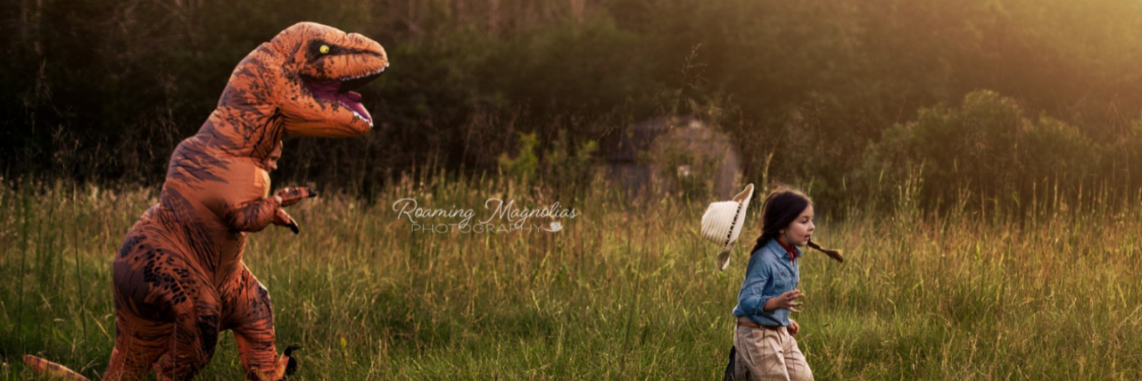 Mom Dresses Autistic Son in T-Rex Costume for Family Photo Shoot A boy in a T-rex costume is chases a girl dressed like a member of Jurassic Park through a field.