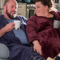 Toby and Kate lounging on a sofa drinking out of mugs.