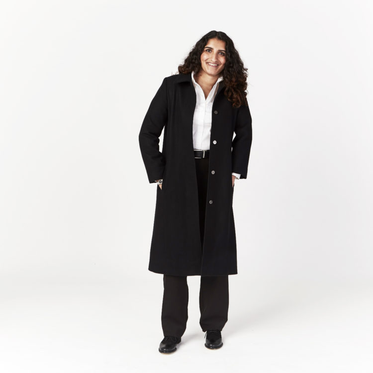 A woman wearing a long black coat with a white shirt underneath and black pants.