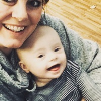 Selfie of mom smiling at camera with 6.5 month old baby with Down syndrome on her lap smiling at the camera, too.
