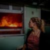 photo of blonde woman looking out of window worried at fire in distance