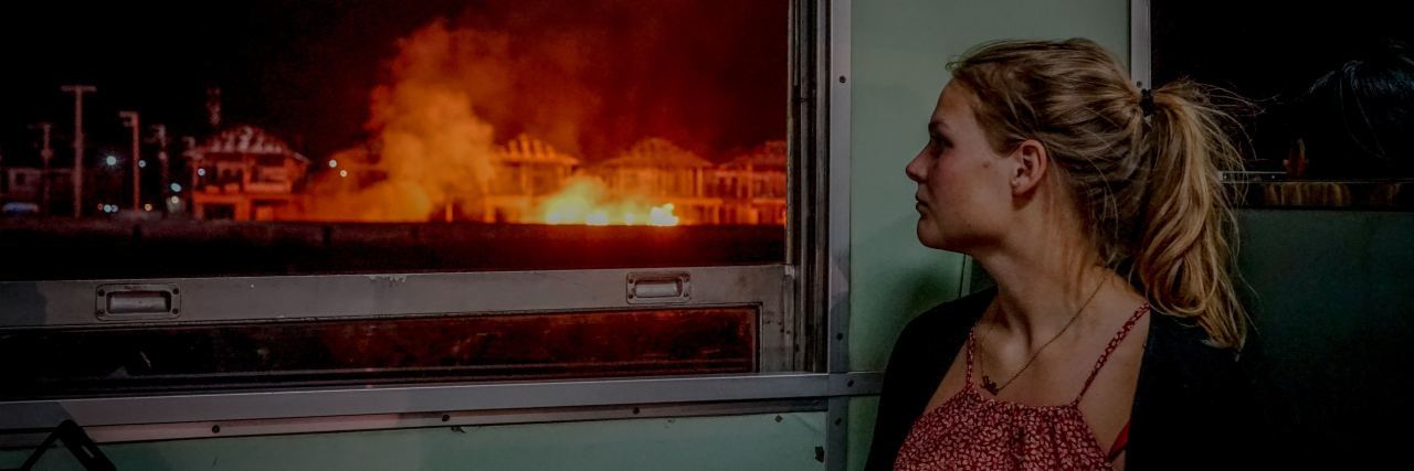 What the Media Doesn't Show About OCD photo of blonde woman looking out of window worried at fire in distance