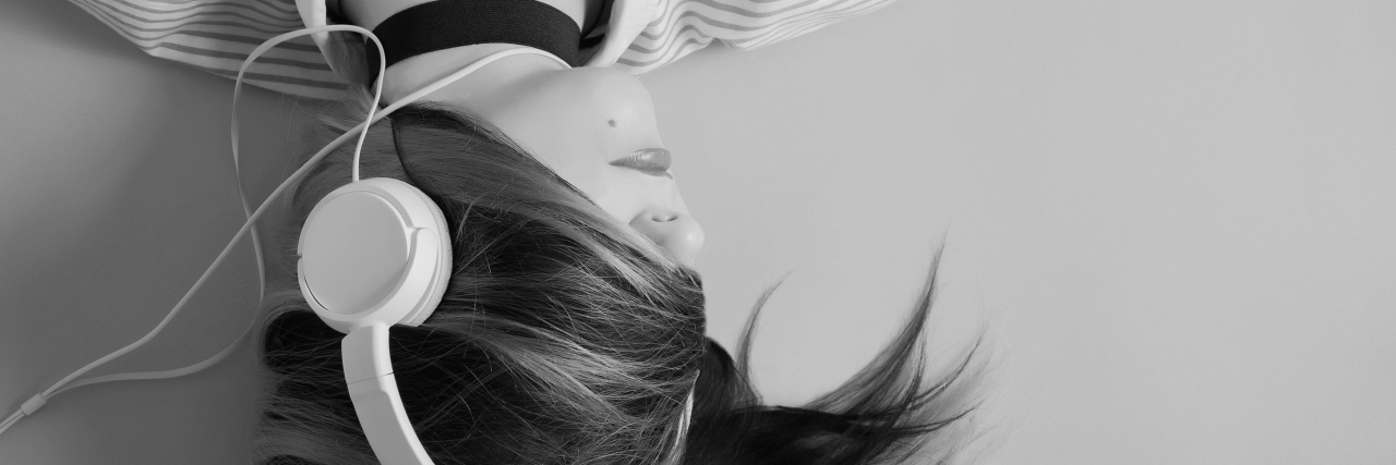 black and white photo of woman with hair covering face lying down and listening to music on headphones