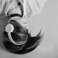 black and white photo of woman with hair covering face lying down and listening to music on headphones