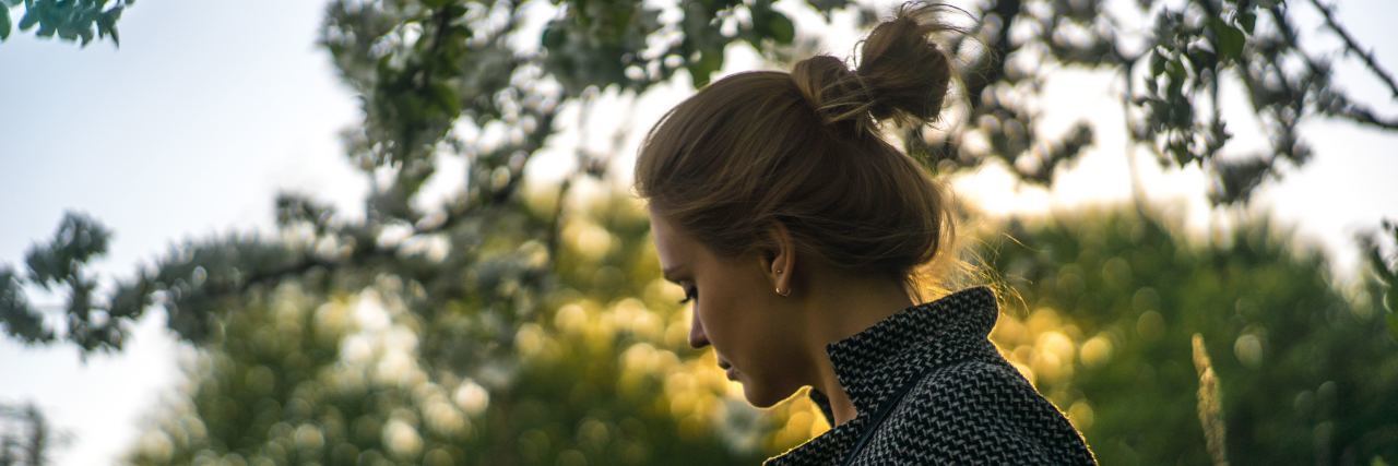 5 Things My Chronic Illness Has Taught Me A woman outside looking away from the camera, trees in the background.