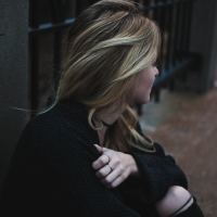 woman with blonde hair wearing a black shirt and sitting outside with her arms crossed, looking away from the camera