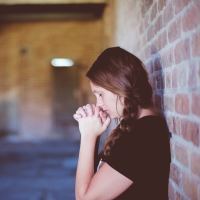 A girl leaning against a brick wall, looking overwhelmed.