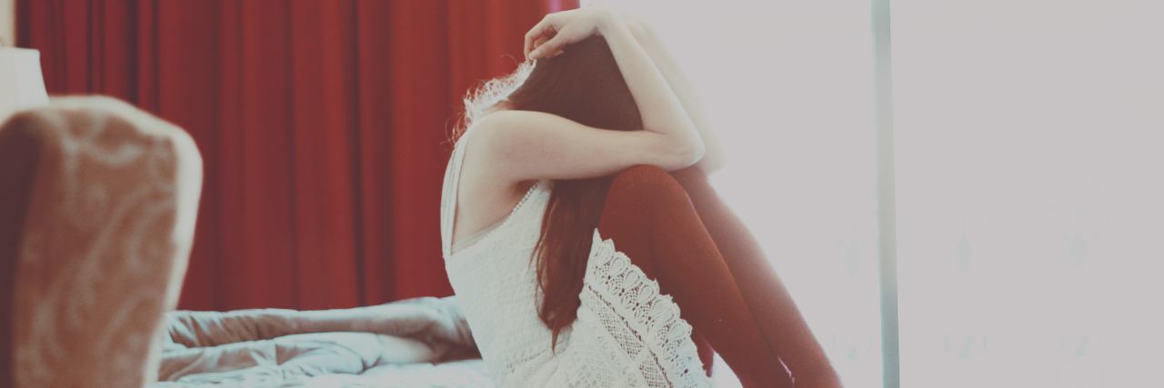 Are People With Psychosis Dangerous? woman sitting on bed with knees raised to face and hiding head scared