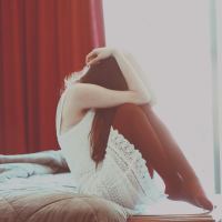woman sitting on bed with knees raised to face and hiding head scared