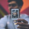man holding polaroid photo of himself in same place