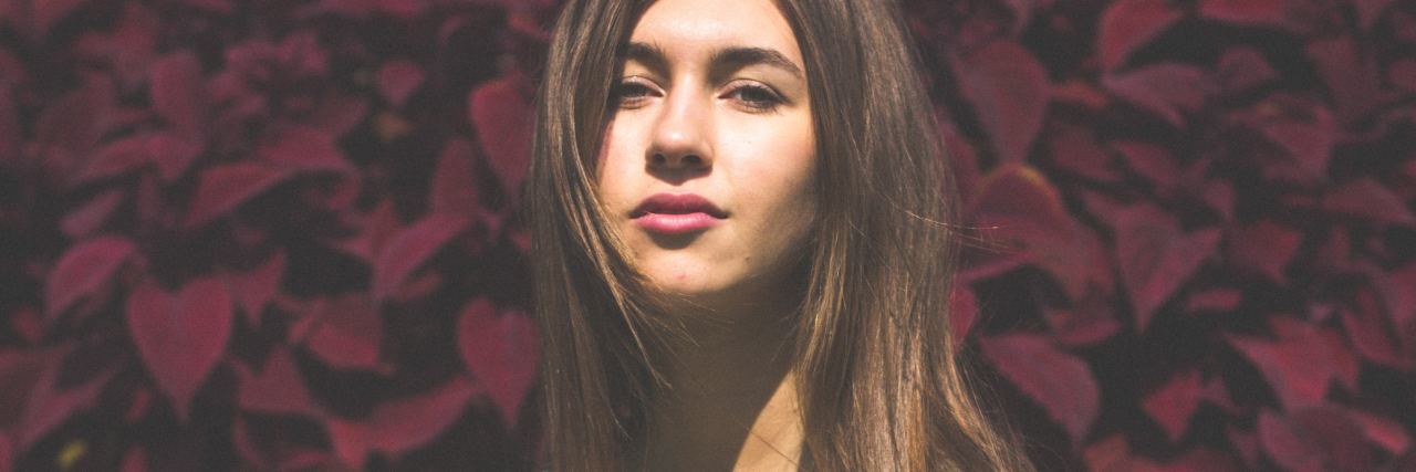 What Others Should Understand About My Chronic Pain woman wearing a mint green dress and sitting in front of red flowers