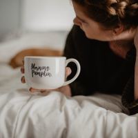 woman lying on bed with "morning pumpkin" mug